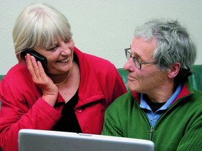 [Translate to COM English:] Elderly couple on front f a laptop looking at each other while she is talking on the phone